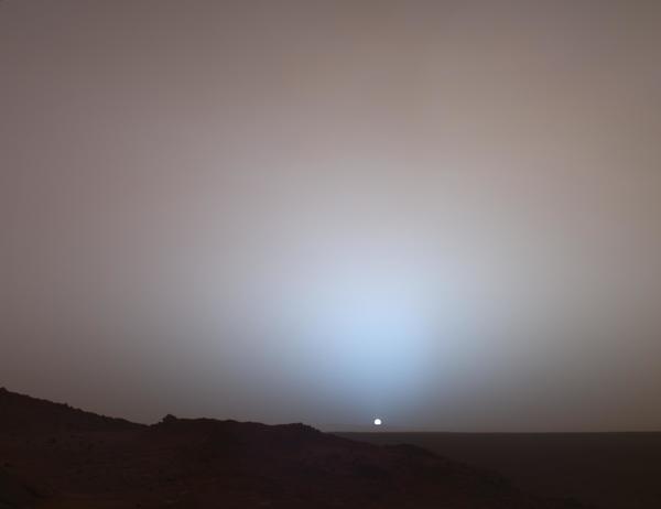 لقطة واسعة لغروب الشمس في "فوهة غوسيف" Gusev، تم التقاطها بواسطة المسبار "روفر" التابع لناسا في عام 2005. نشاهد فيها هالةً زرقاء وسماءً ورديّة اللّون، وذلك بسبب طبيعة غبار المريخ الناعمة