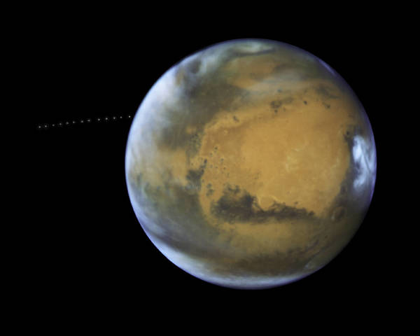 علي مدى 22 دقيقة، ألتقط هابل 13 صورة مختلفة بتقنية التعريض الطويل، مما سمح لعلماء الفلك بصنع صورة بتقنية الزوال الزمني ليوضح حركة القمر فوبوس خلال مداره (النقطة البيضاء) حول المريخ، وتلك الصورة مكونة من صور ذات تعريض طويل مختلفة اخذها مقراب ناسا الفضائي هابل عن طريق اجهزته WFC3/UVIS ،  المصدر : ناسا، وكالة الفضاء الأوربية، معهد علوم تلسكوب الفضاء وشكر موجه لـ ج.بيل ( جامعة اريزونا) و م. ولف (معهد علوم الفضاء)